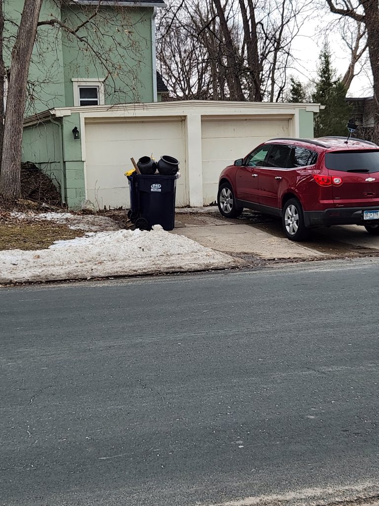 A two car garage behind a trash bin with two cauldrons overflowing out the top.