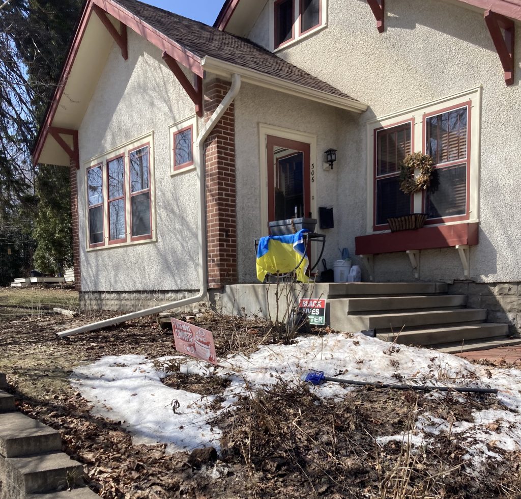 house with yard signs and Ukraine flag out front. some snow still on the ground.