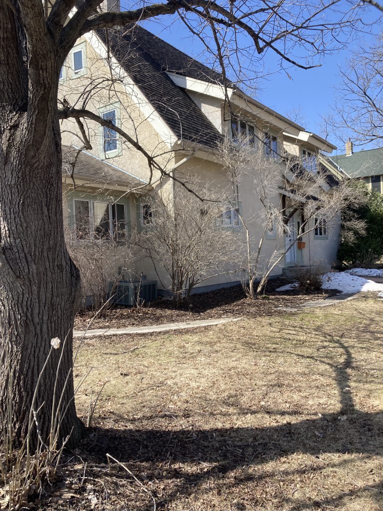 There is a two or three story stucco-inspired house slightly obscured by a leafless tree.