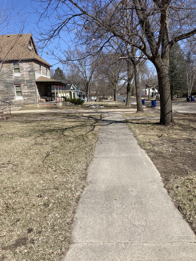 A sidewalk stops after one house. In the distance there is a small chunk of sidewalk.