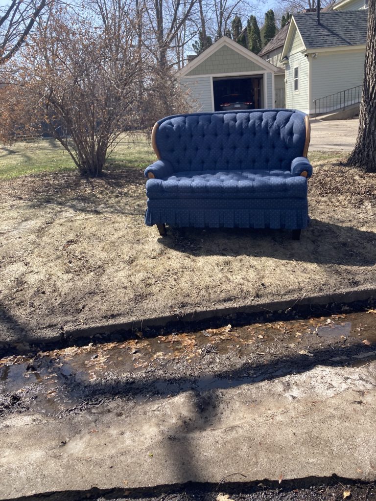 A blue couch sits by the side of the road.