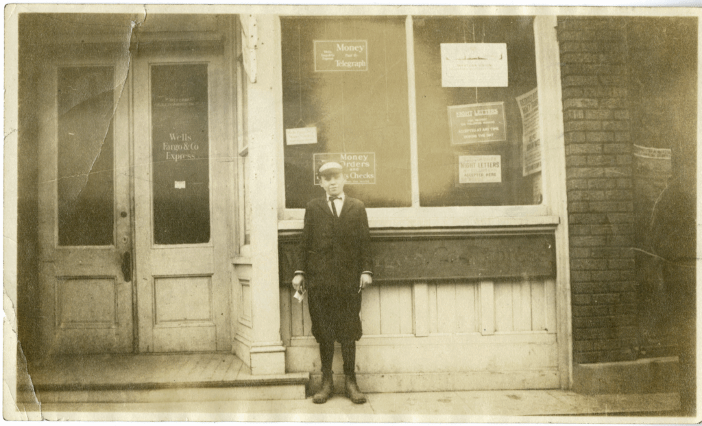 Black and white image of a young boy standing in front of old Wells Fargo office