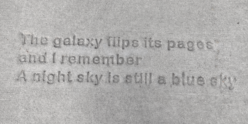 Poem stamped into sidewalk, reads: "The galaxy flips its pages/ and I remember/ a night sky is still a blue sky."